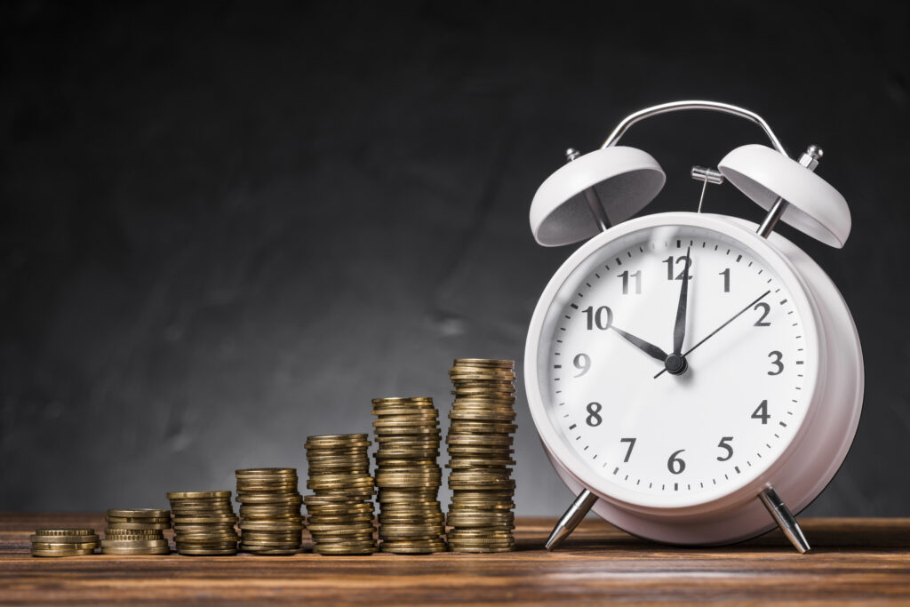 stack-increasing-coins-with-white-alarm-clock-wooden-desk-against-black-background